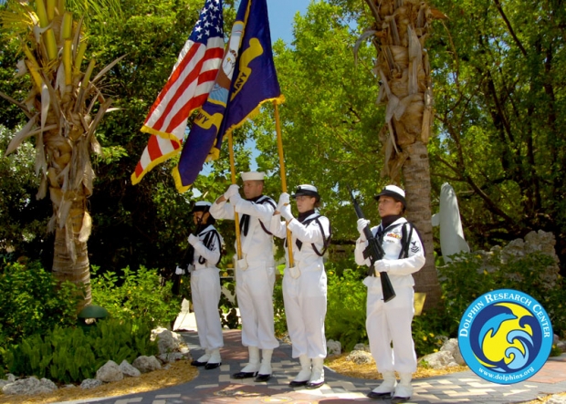 A military color guard in front of some pine trees