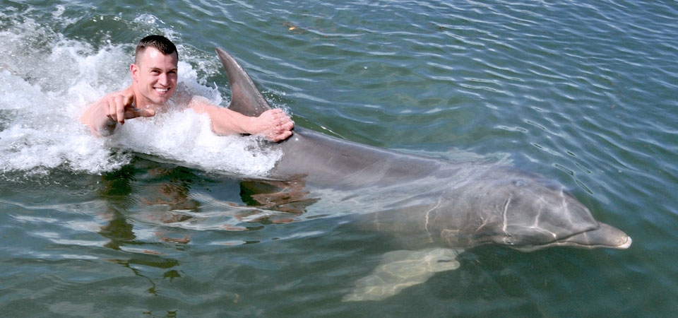 A man waves to the camera while being pulled by a dolphin's dorsa