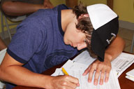 Student writing on some worksheets (Program Image)