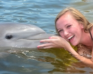 Woman getting a kiss from a dolphin in the water.